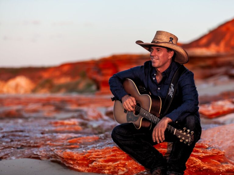 Tom Curtain with his guitar framed by the red rocks of the outback.
